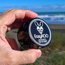 Hand holding a black EasyROO grinder by GrinderROO with a beach in the background