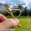 Two gold and titanium herb scoops held by a hand with a blurred outdoor background.