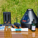 Vaping device, accessories, and cleaning products on a wooden table with grass in the background
